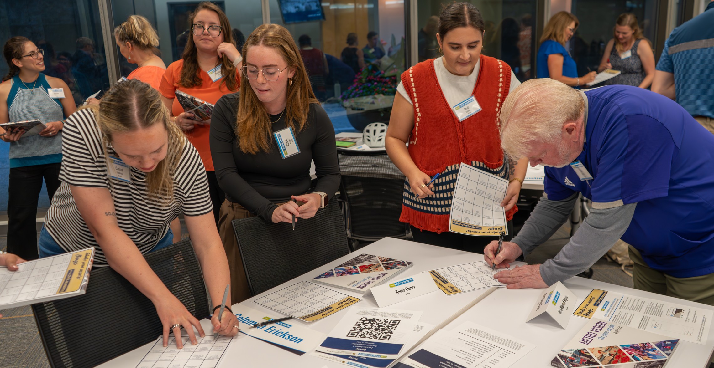 A group of people standing while filing out forms in a conference room.