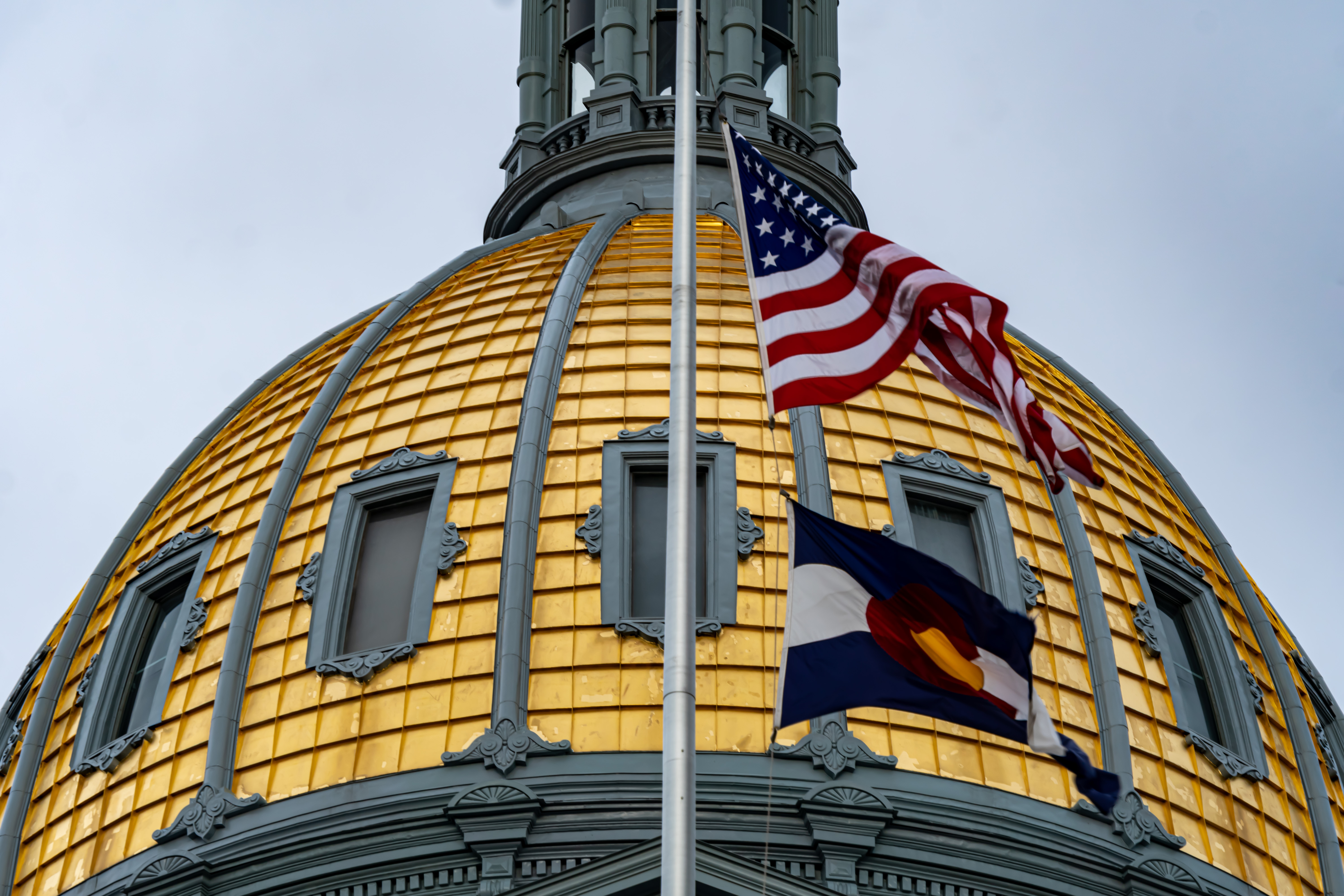 A close-up of Colorado's gold-domed capitol, with the American and Colorado flags in the foreground.