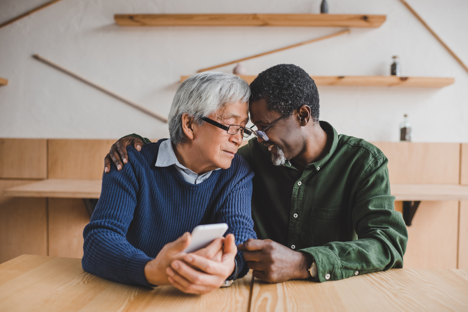 An older adult man of Asian descent and an older adult man of Black descent embrace each other.
