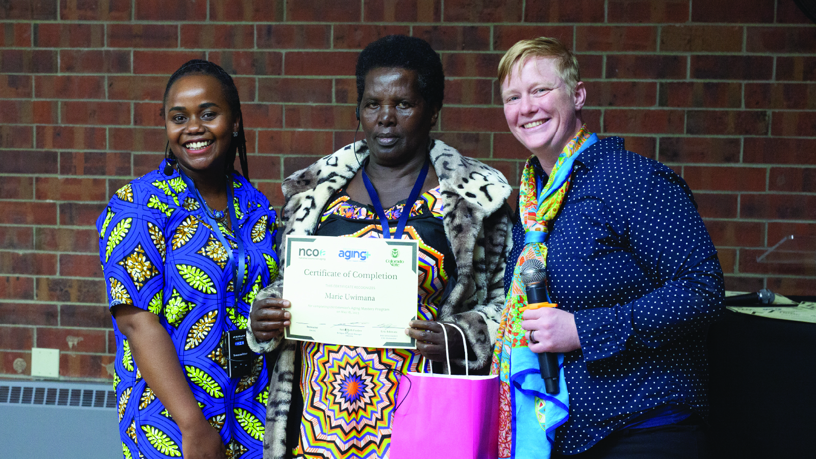 Older adult refugee woman, center, holds a certificate from the program along side two staffers in the program.