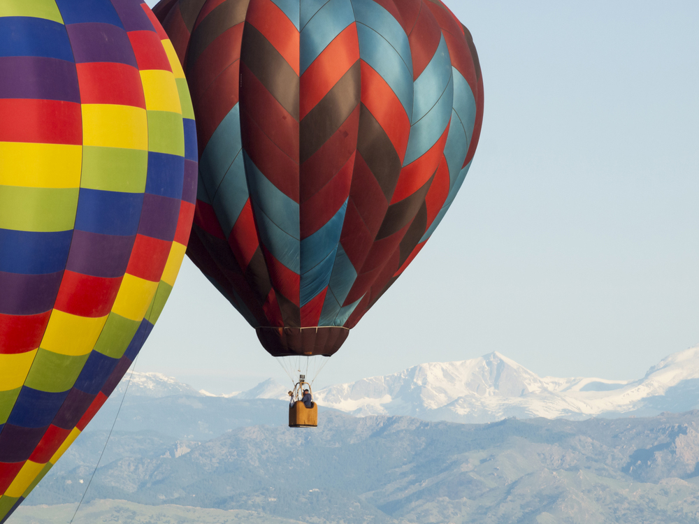 Hot air balloons over Erie, Colorado, with snow-covered foothills beyond.
