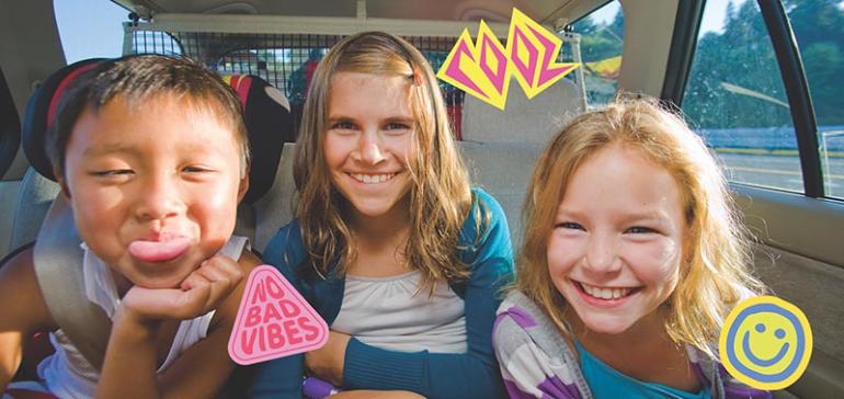 Three kids smiling in the backseat of a car.