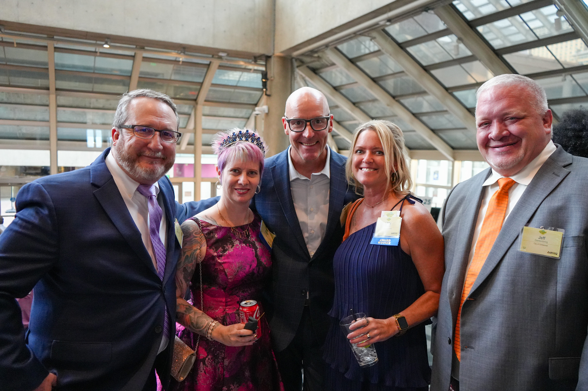 A group of five smiling white people in business casual attire under atrium windows.