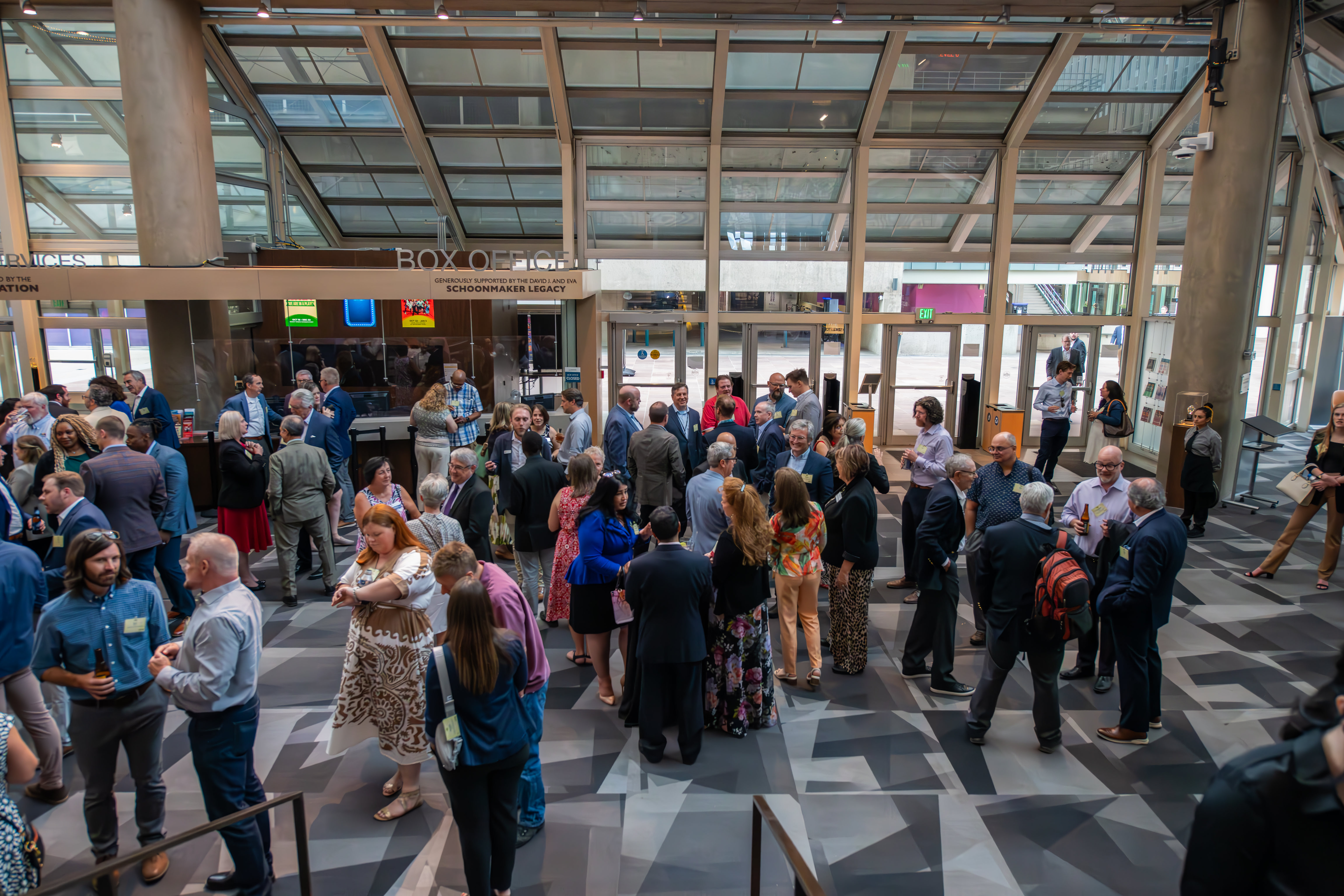 A large group of people, dressed in celebratory casual attire, mingle in the lobby of the Denver Center of the Performing Arts.