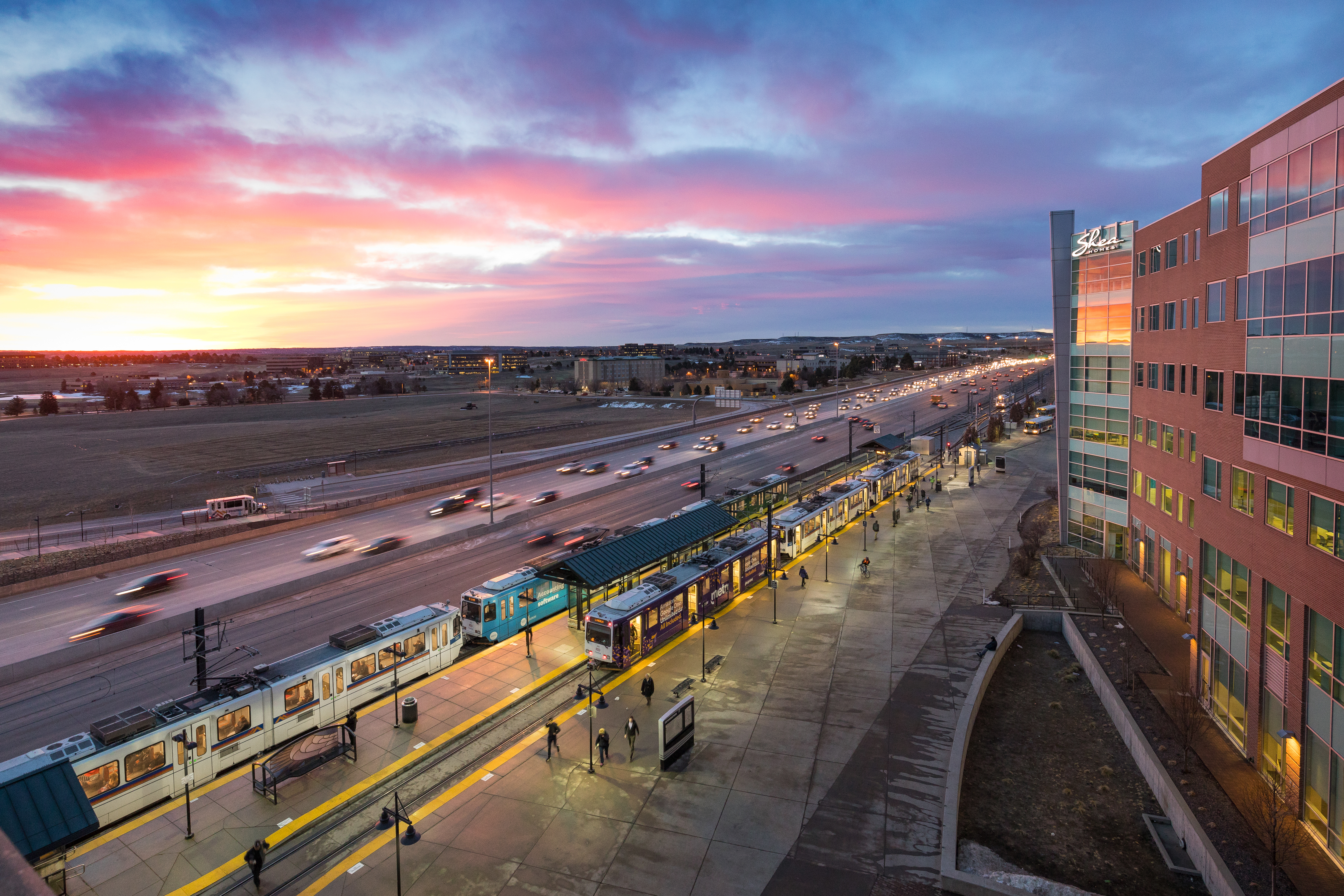 Light rail at Lincoln Station with vehicles traveling on the interstate in the foreground.