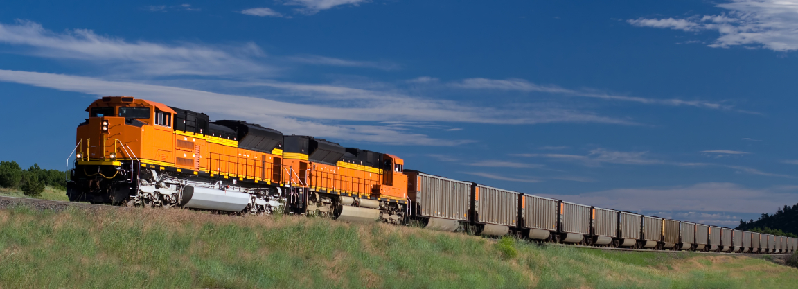 A freight train travels through the prairie under a blue sky.