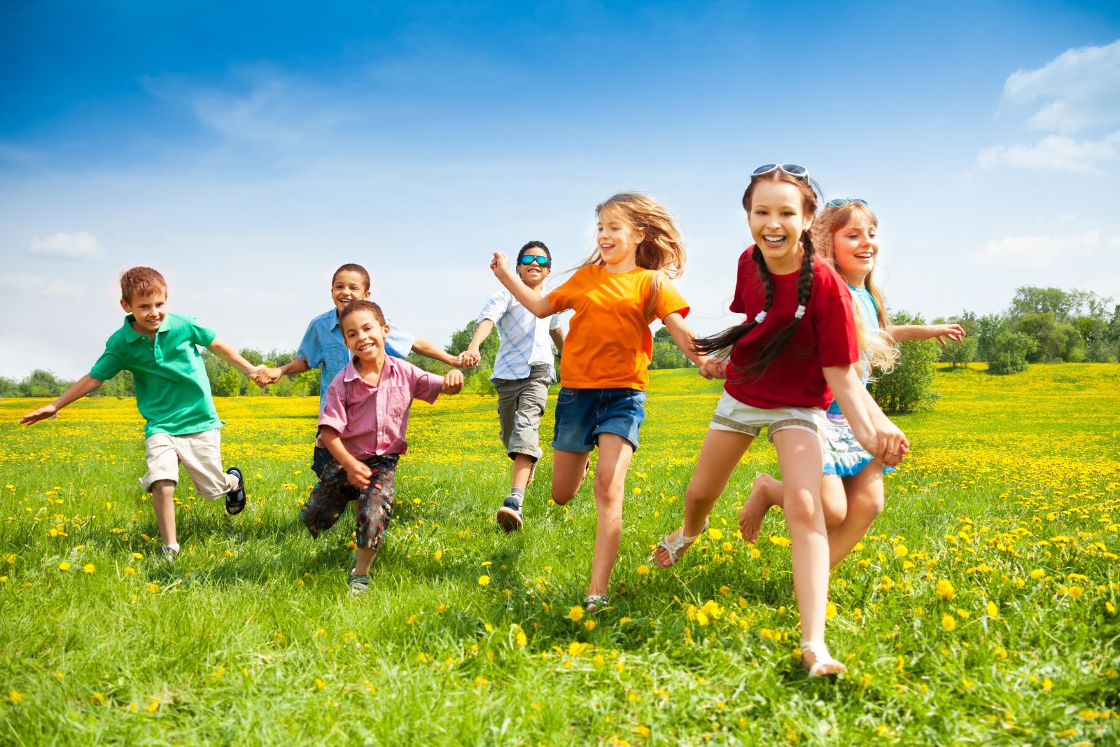 A group of children running through a vibrant, green field with blue skies in the background.