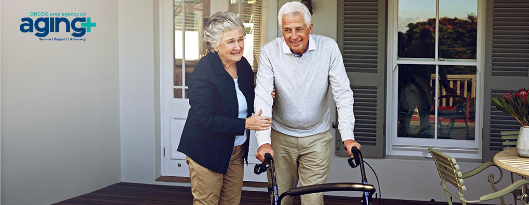 An older adult woman walks on the porch with a older adult man who uses a walker.