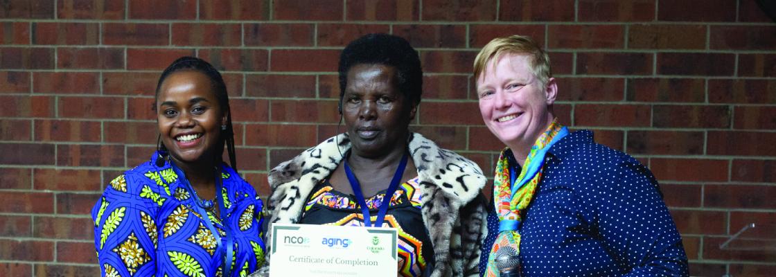 Older adult refugee woman, center, holds a certificate from the program along side two staffers in the program.