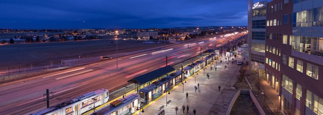 People walking around a light rail station at night with a highway in the background. Photo credit: Photo courtesy of RTD.