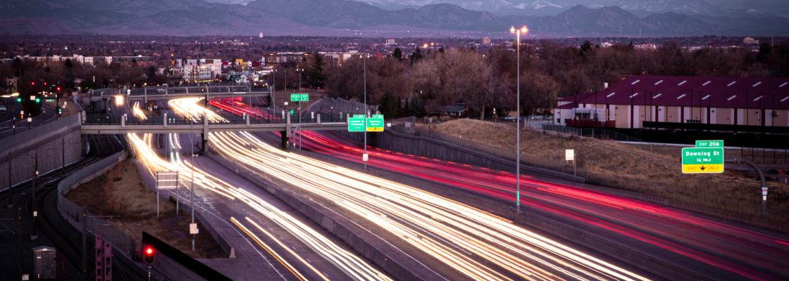 Cars on a highway at dusk with motion blur headlights and mountains in the background.