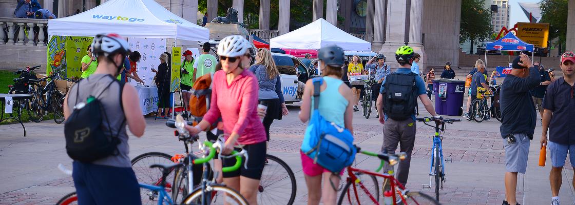 Four bicyclists standing with their bicycles in the center of Civic Center Plaza in Denver, Colorado while in the foreground are several white tents where people are receiving free gift bags.