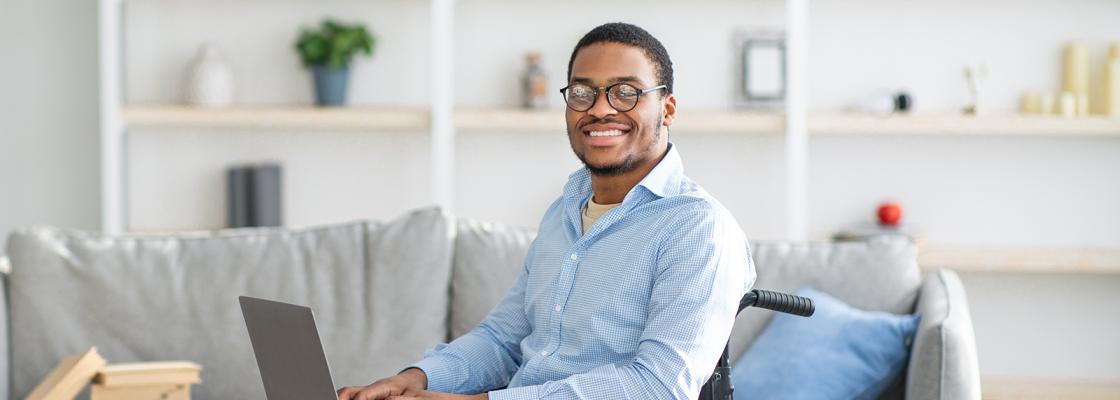 A young professional Black man using a wheelchair works at home using a laptop.