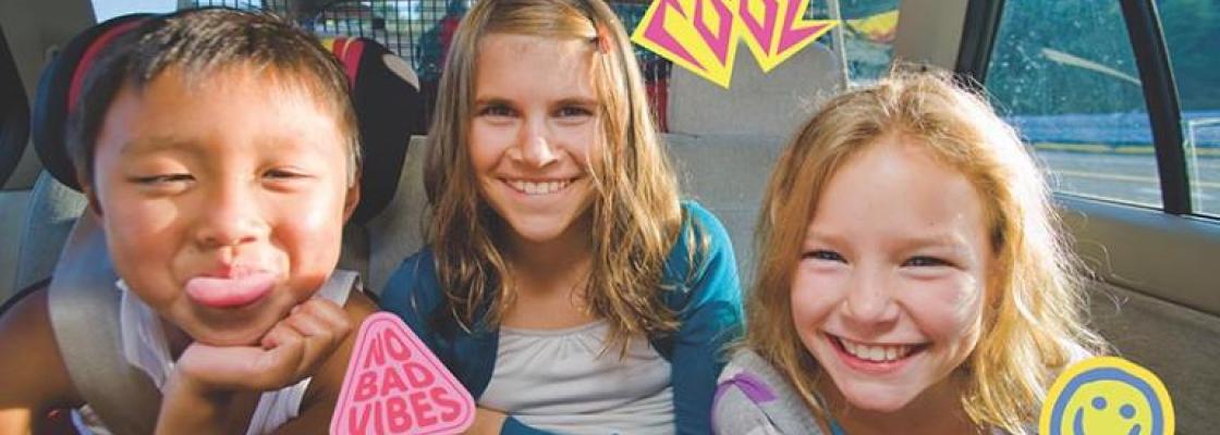 Three kids smiling in the backseat of a car.