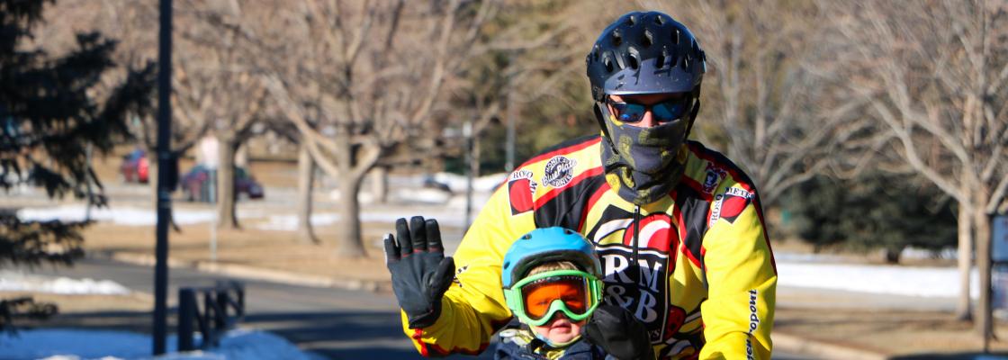 A young child rides bicycle with and adult with snow on the ground.