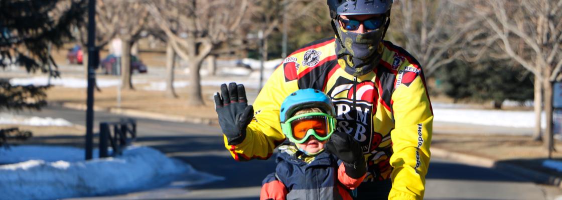 A young child rides bicycle with and adult with snow on the ground.