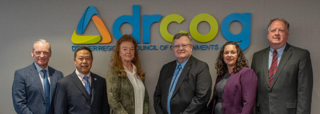 A diverse group of six people stand shoulder-to-shoulder in a conference room.