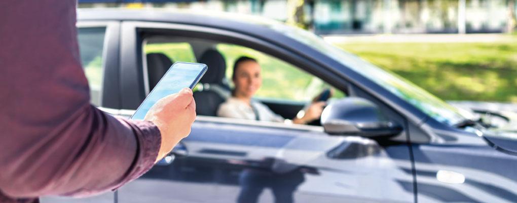 A person holding a mobile phone checks the identity of the rideshare driver by comparing the information on the mobile phone.